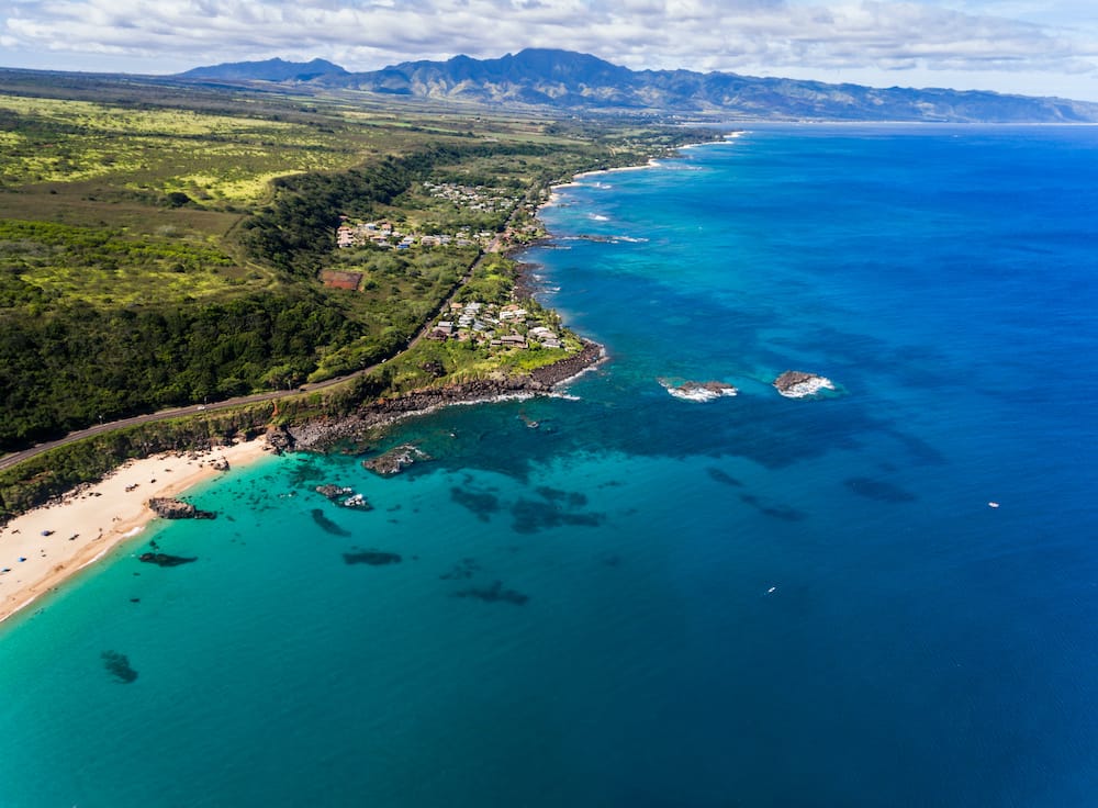 An aerial view of the rocky coastline and white-sand beaches and pure blue water on the North Shore of Oahu.