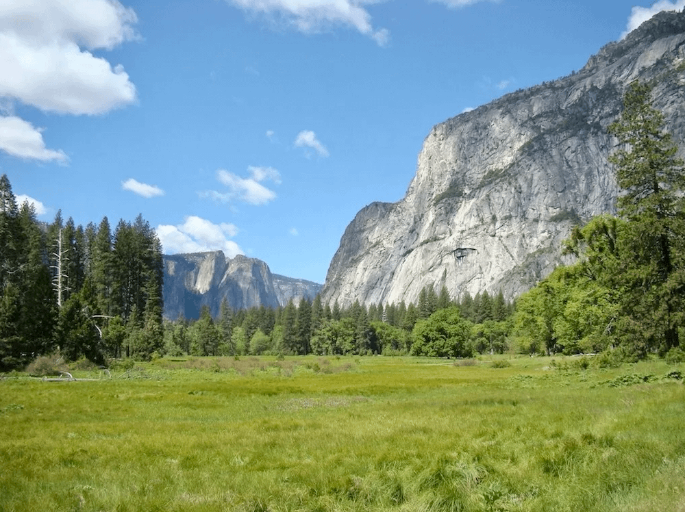 The stone mountains, green fields, and trees in Yosemite National Park in May - one of the best places to visit in the USA in 2023.