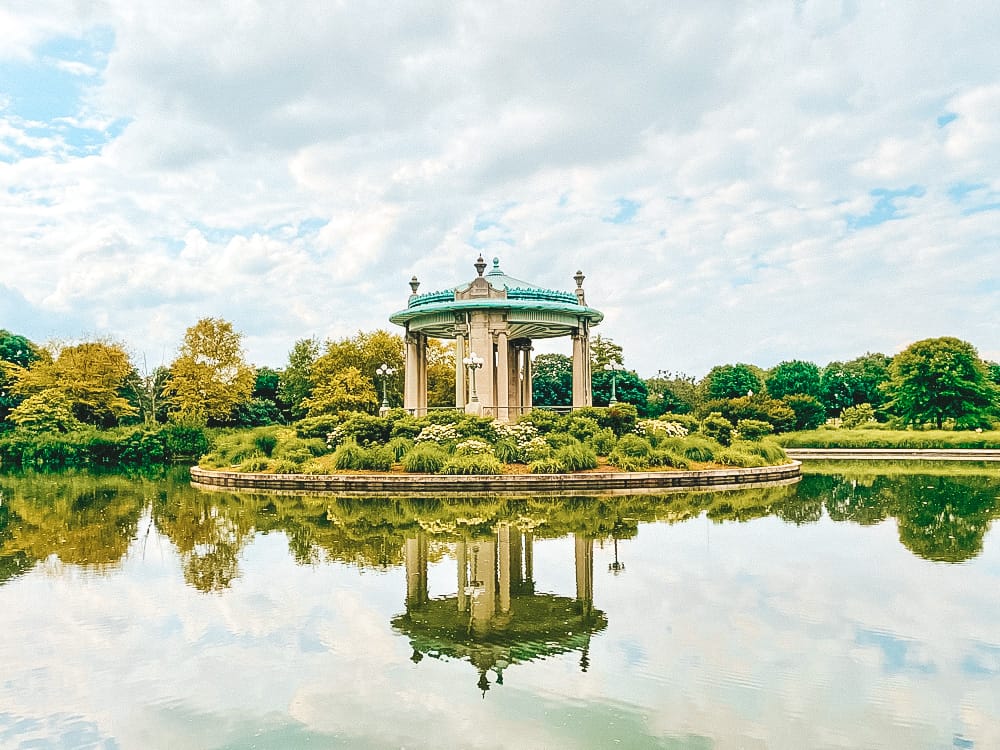 A domed arch in a park in St. Louis with a copper roof surrounded by greenery and a lake.
