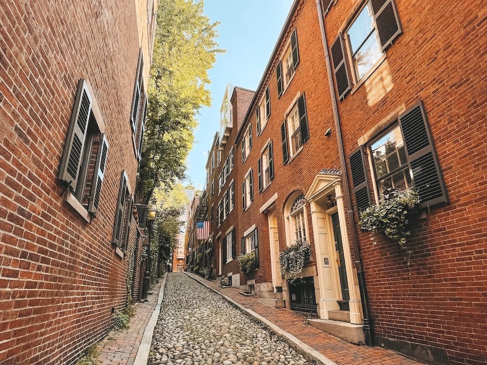 Cobblestone streets, red brick buildings, and an American flag in Acorn Street in Boston, MA.