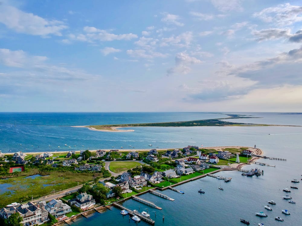 An aerial view of a green, marshy peninsula with gorgeous homes, private e docks, and the ocean in the background.