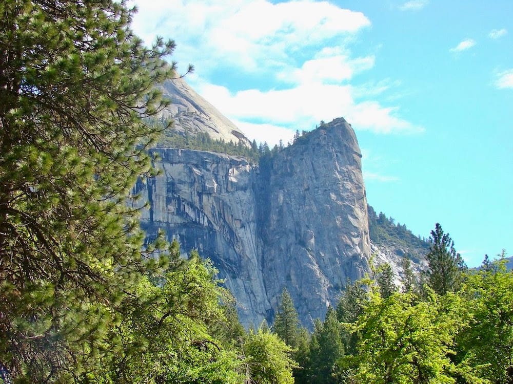 A granite cliff in Yosemite National Park with green trees and a blue sky in the background.