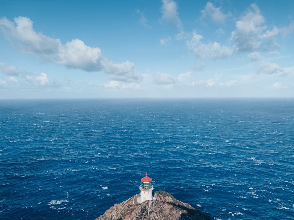 A red and white lighthouse sitting on the edge of a cliff and overlooking the blue Pacific Ocean