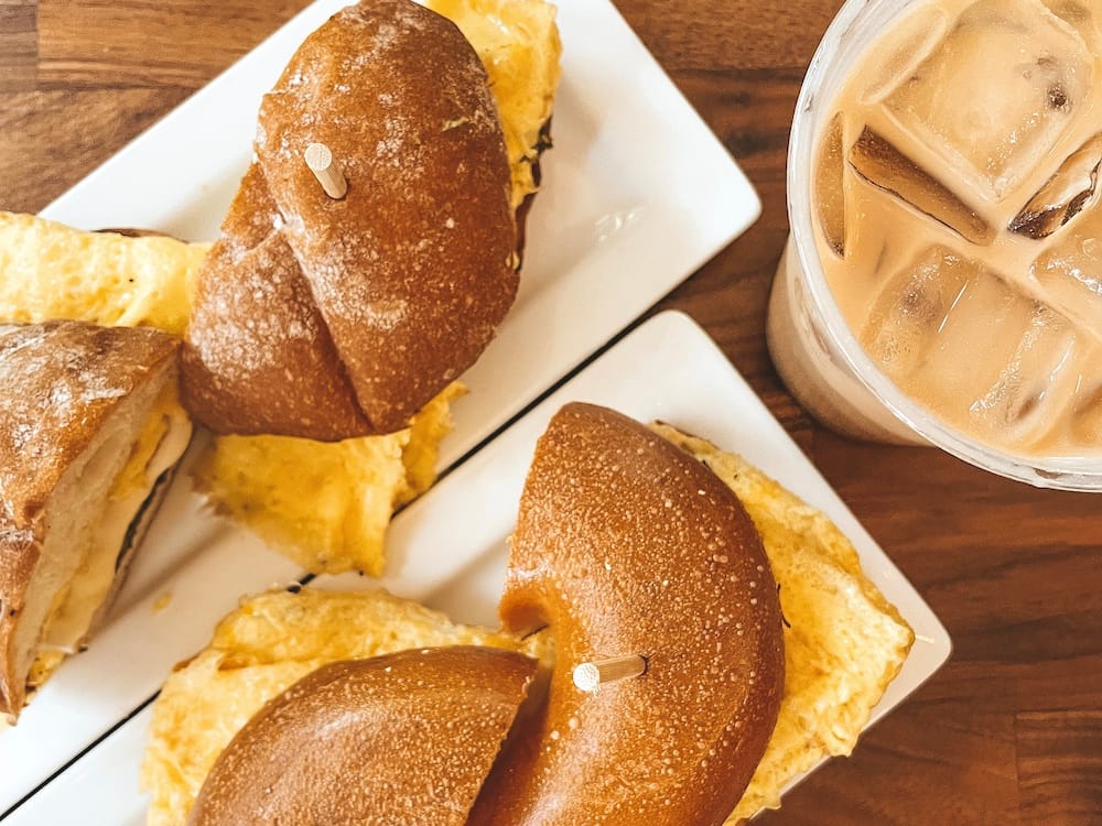 Two breakfast sandwiches and an iced coffee sitting on a wooden table
