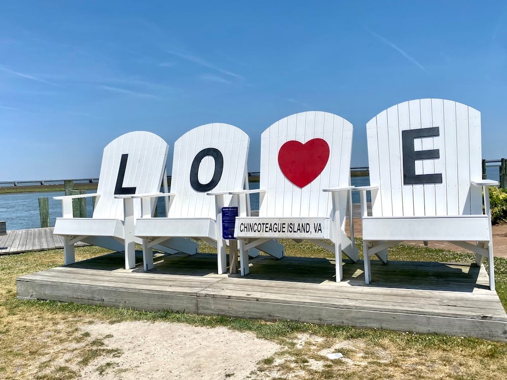 Four giant white beach chairs with black letters spelling "LOVE". The "V" is a red heart.