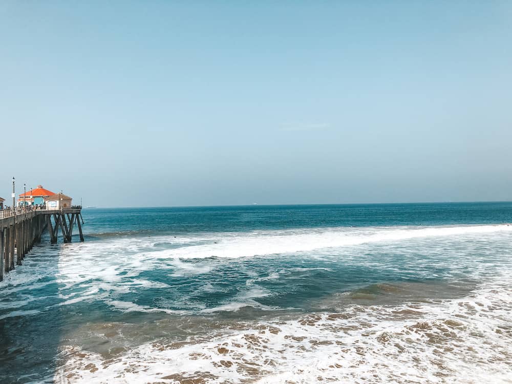 The blue ocean with a pier and a red restaurant at the end of a boardwalk at Huntington Beach