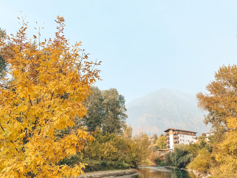 Mountains and a white and brown building at the end of a river in Leavenworth, Washington, framed by yellow and green trees in October.