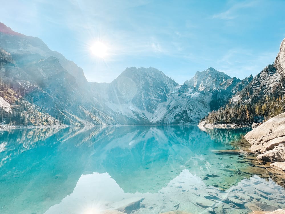 A view of a blue alpine lake surrounded by mountains and larch trees.