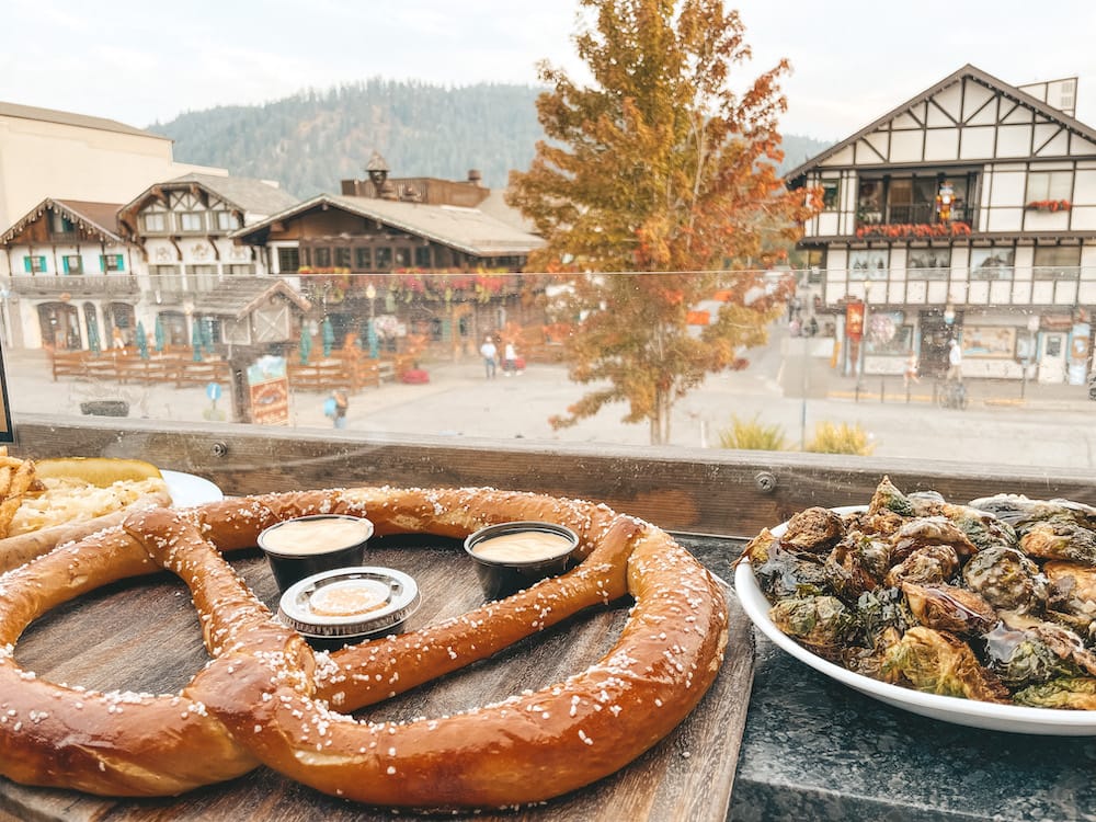 A large pretzel, Brussels sprouts sitting on a table in front of Downtown Leavenworth.