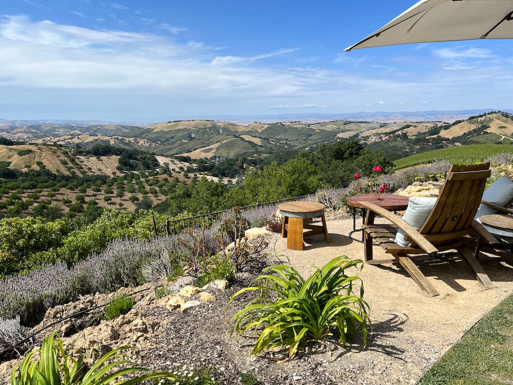 A wooden chair on a cliff sitting and overlooking the lush green vineyards is Paso Robles during harvest season in October.