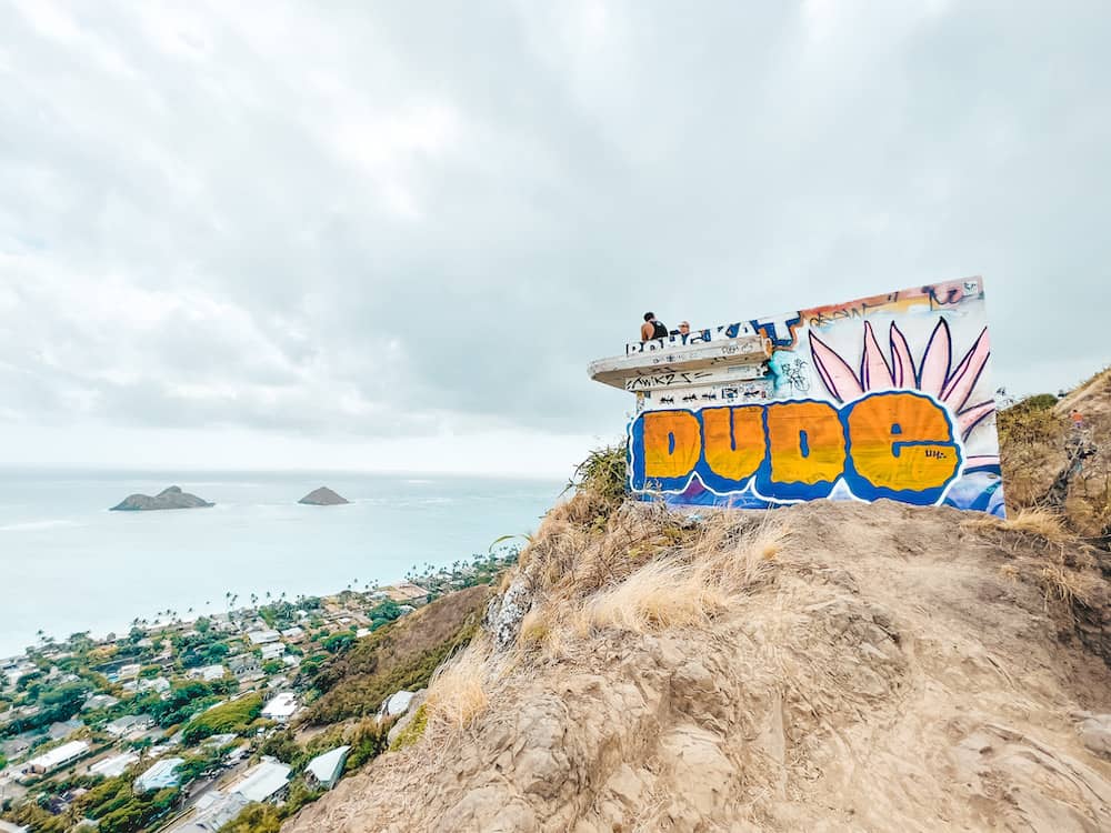 The pillbox on the Lanikai Pillbox Hike at the top of the mountain with "Dude" spray painted in orange and blue letters on the side overlooking the ocean.
