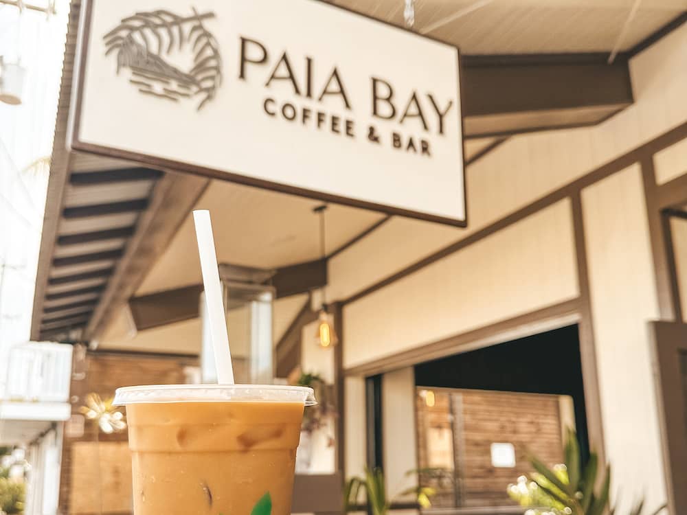 An iced coffee in front of the sign for Paia Bay Coffee Bar, one of the best places to eat in Maui.