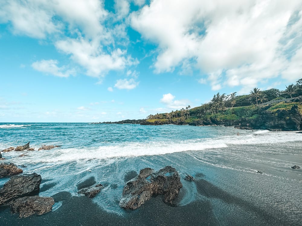 A black sand beach in Hawaii with turquoise waters and lush greenery surrounding the beach