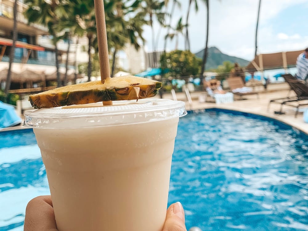 A hand holding a pina colada in a plastic cup by the pool at Outrigger Resort Waikiki Beach.