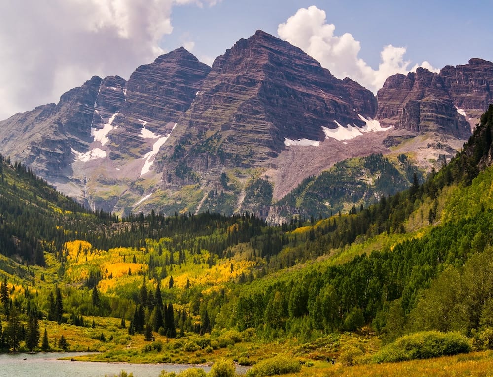 The massive mountain ranges with snow and yellow and green fall ground cover in Aspen, Colorado, in October.