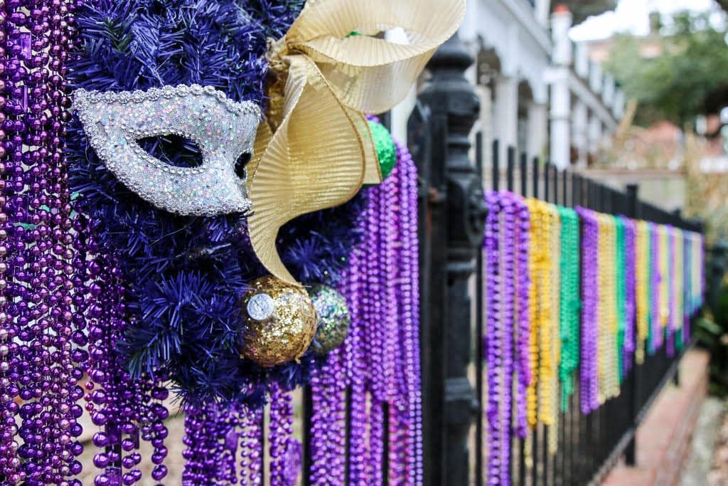 Tons of purple, gold, green beads hanging on a black fence and a masquerade mask from Mardi Gras.