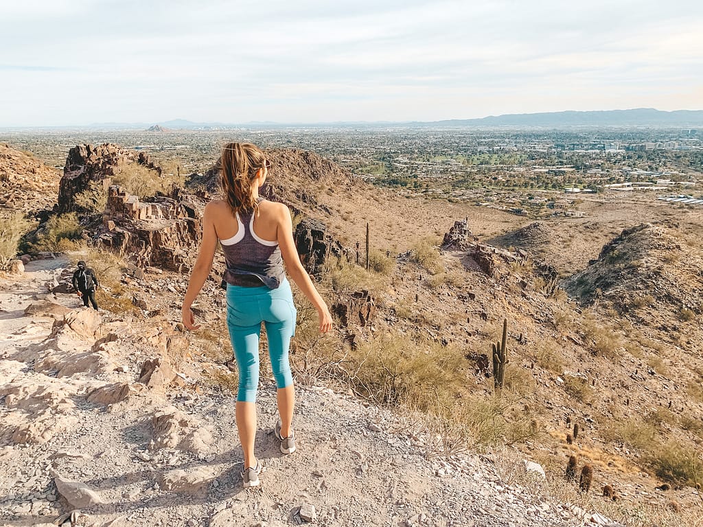A woman in a gray tank top and green leggings standing and overlooking the desert in Phoenix, Arizona on the Piestewa Peak Trail.