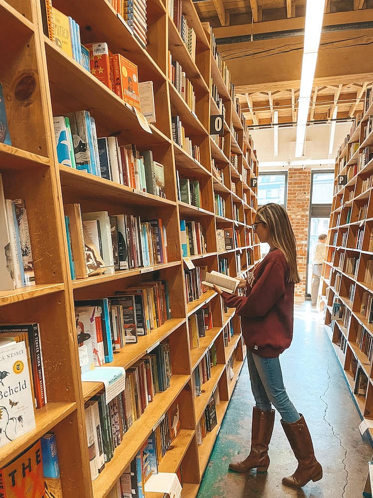 A woman reading a book in between the shelves of a bookstore in Portland.