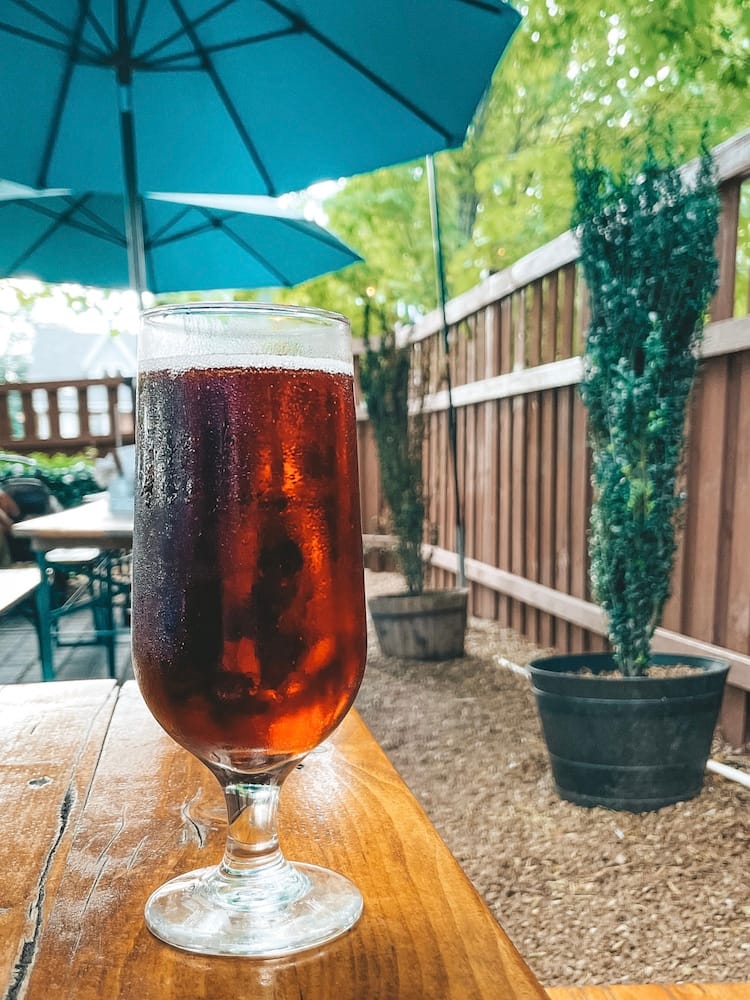 A cider sitting on a table at a beer garden with blue umbrellas and a brown fence in the background