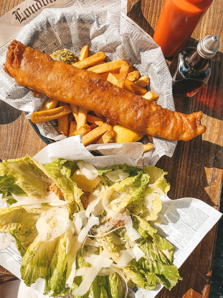 Fish and chips and a ceasar salad sitting on a table.
