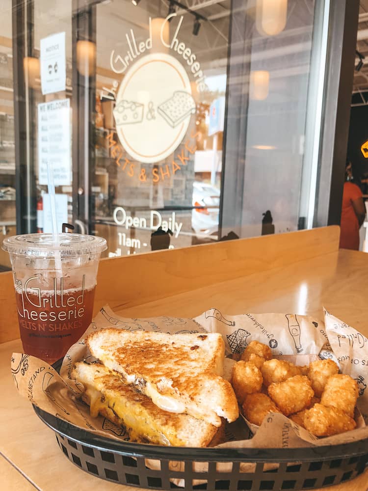 A basket with a grilled cheese and tater tots and an iced tea sitting on the table