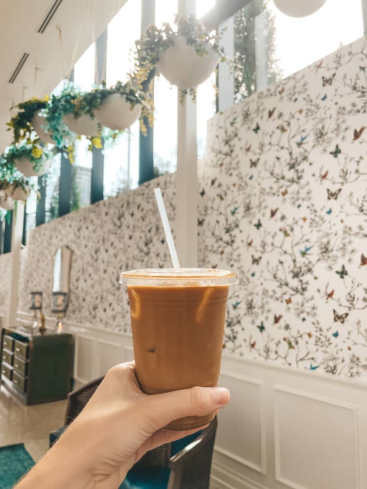 An iced coffee with butterfly wallpaper and greenery in the background