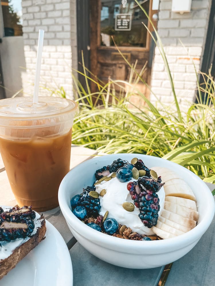 An iced coffee and bowl of granola, fruit, and yogurt sitting on an outside table
