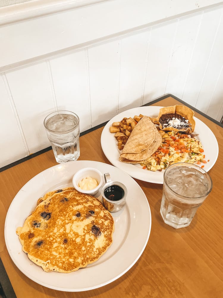 La Jolla or Coronado: Two plates with pancakes, eggs, beans, tortillas, and breakfast potatoes sitting on a wood table with two glasses of water.