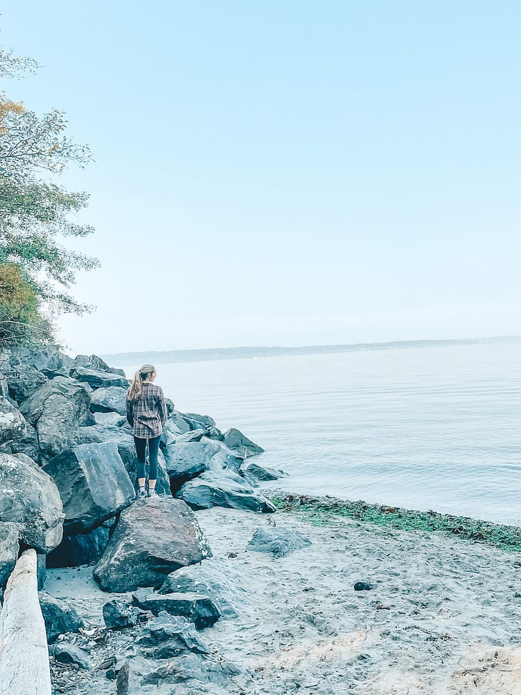 A woman standing on a rock on a beach in Seattle.