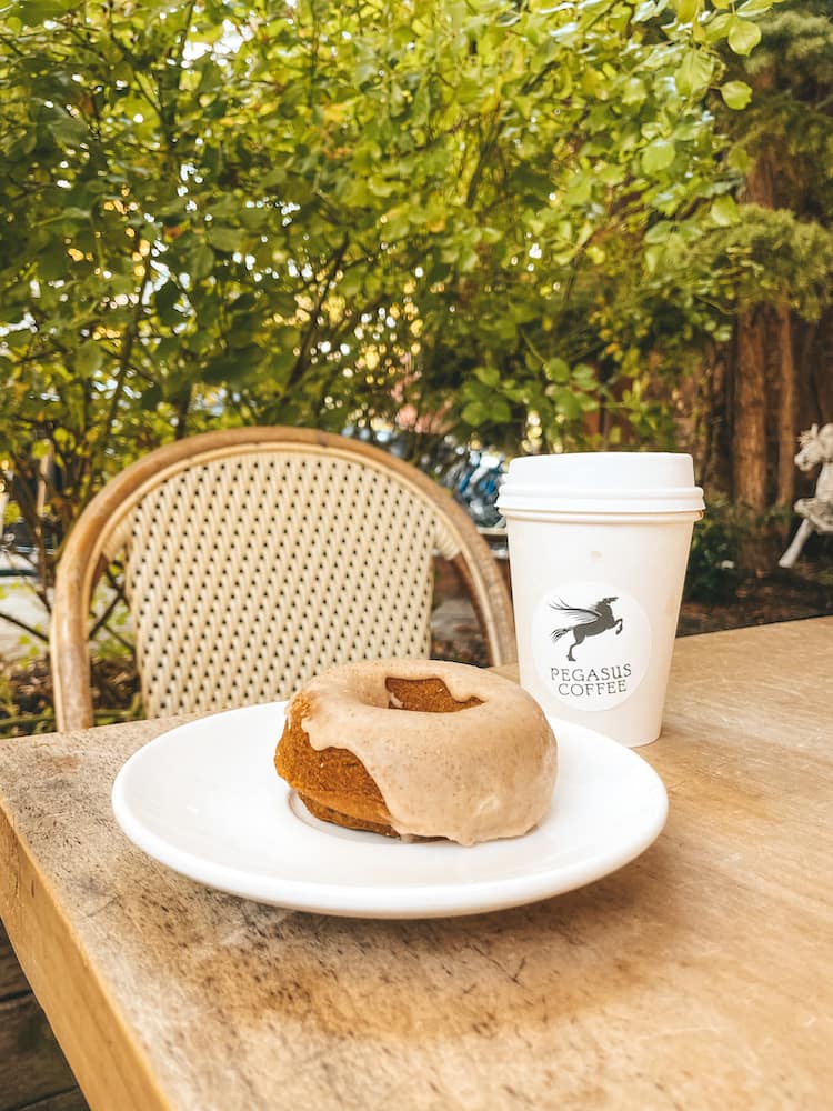 A donut and a cup of coffee sitting on a wooden table with a green backdrop