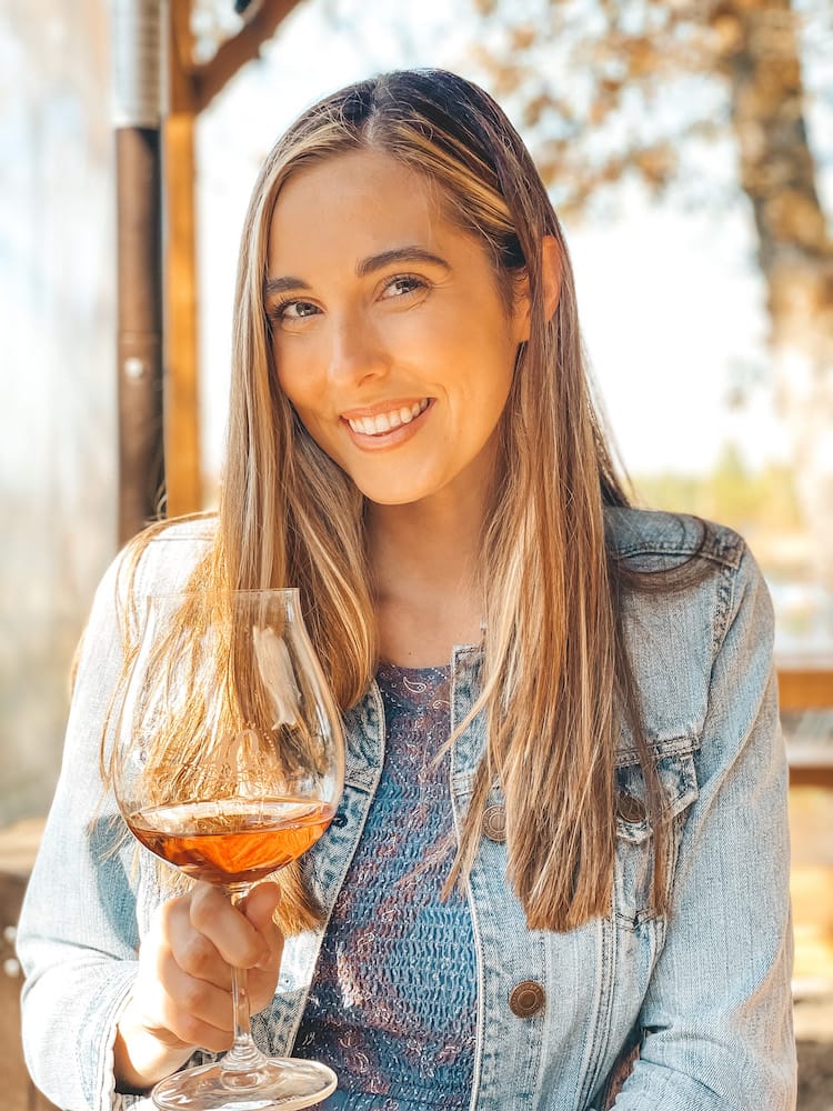 A woman with long brown hair holding a glass of pink sparkling wine.