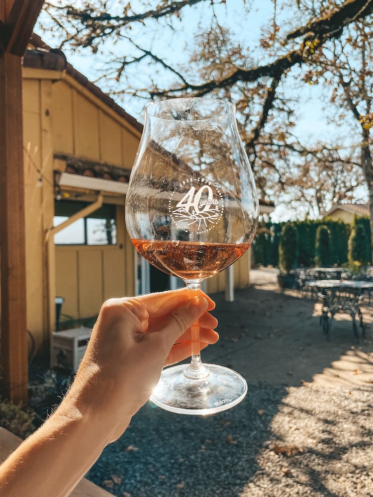 A glass of pink sparkling wine in front of a farmhouse and tree.