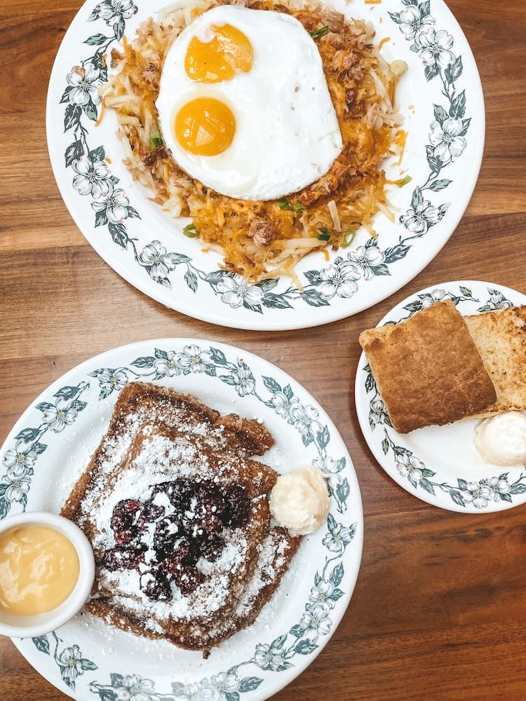 A breakfast sitting on a wood table with eggs, hashbrowns, and French toast