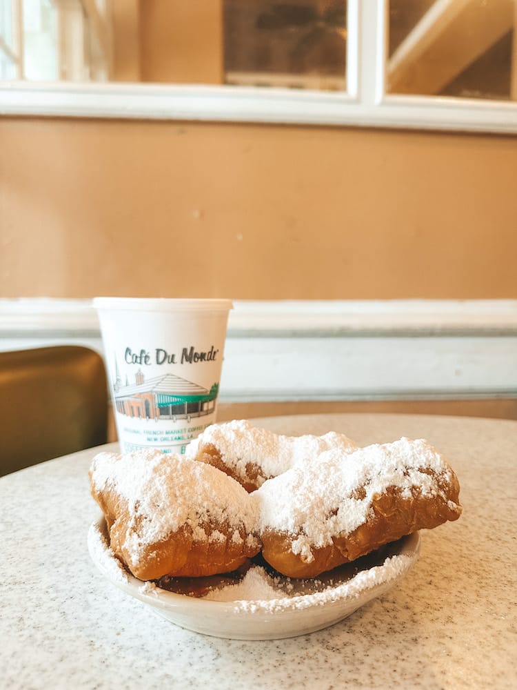 A plate of beignets and a coffee in a white cup that reads "cafe Du Monde"