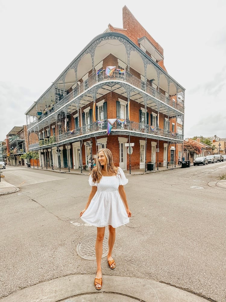 A woman in a white dress standing in front of a unique apartment building with metal railing in the French Quarter in New Orleans.