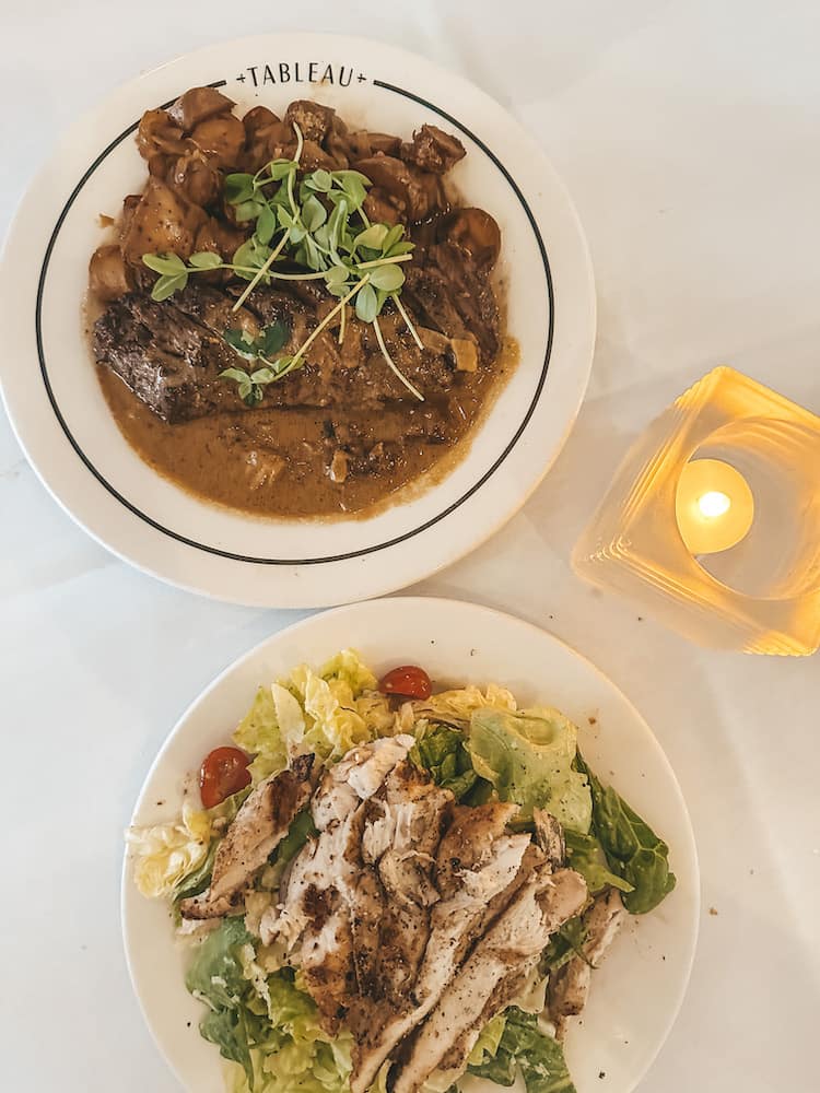 Two plates of food, one a steak with mushrooms and the other a chicken salad.