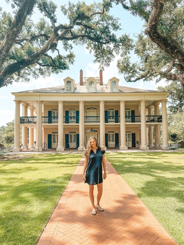 A woman in a black dress is standing in front of a historic building on a plantation on a red brick sidewalk.