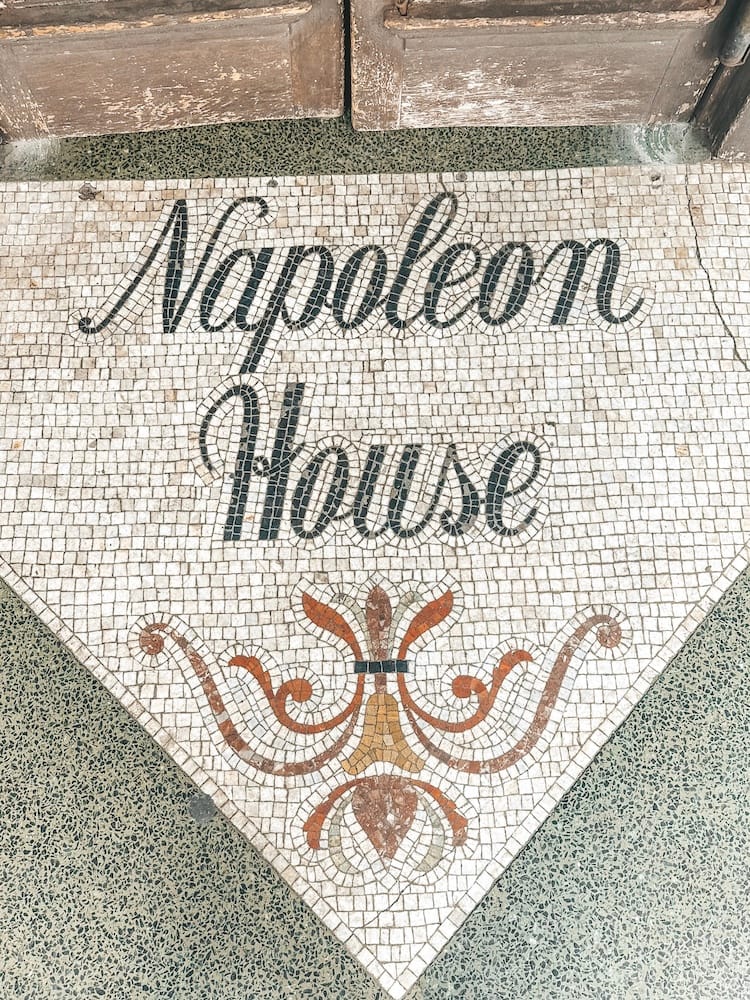 The words "Napoleon House" are in a tile mosaic on a sidewalk on a corner in New Orleans in front of a restaurant.