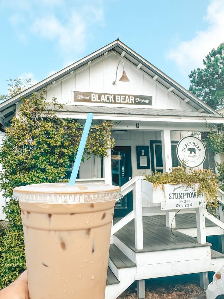 An iced coffee with a blue straw in front of a while building with greenery on the outside. Black Bear Bread Company - one of the best things to do in Grayton Beach