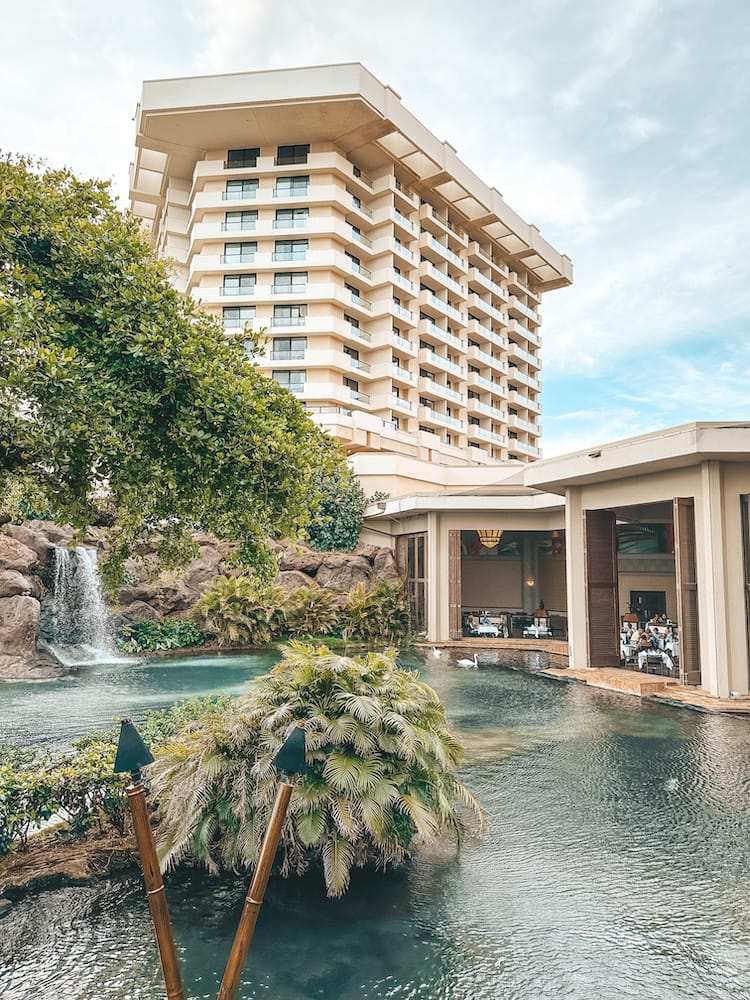 A hotel tower overlooking a lake, greenery, and waterfall at one of the best luxury resorts in Maui.
