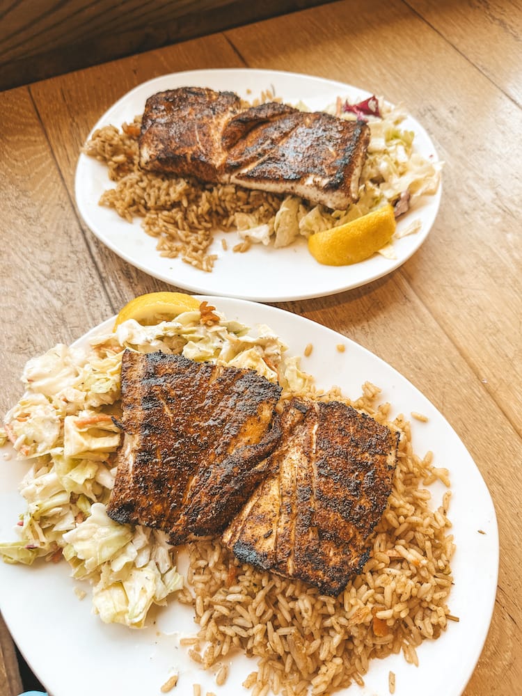 Two plates with fish filets, rice, and coleslaw sitting on a wooden table.