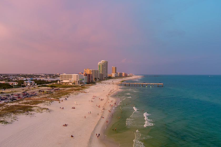 A view of the skyline of Orange Beach Alabama at sunset with a pink sky and blue water.