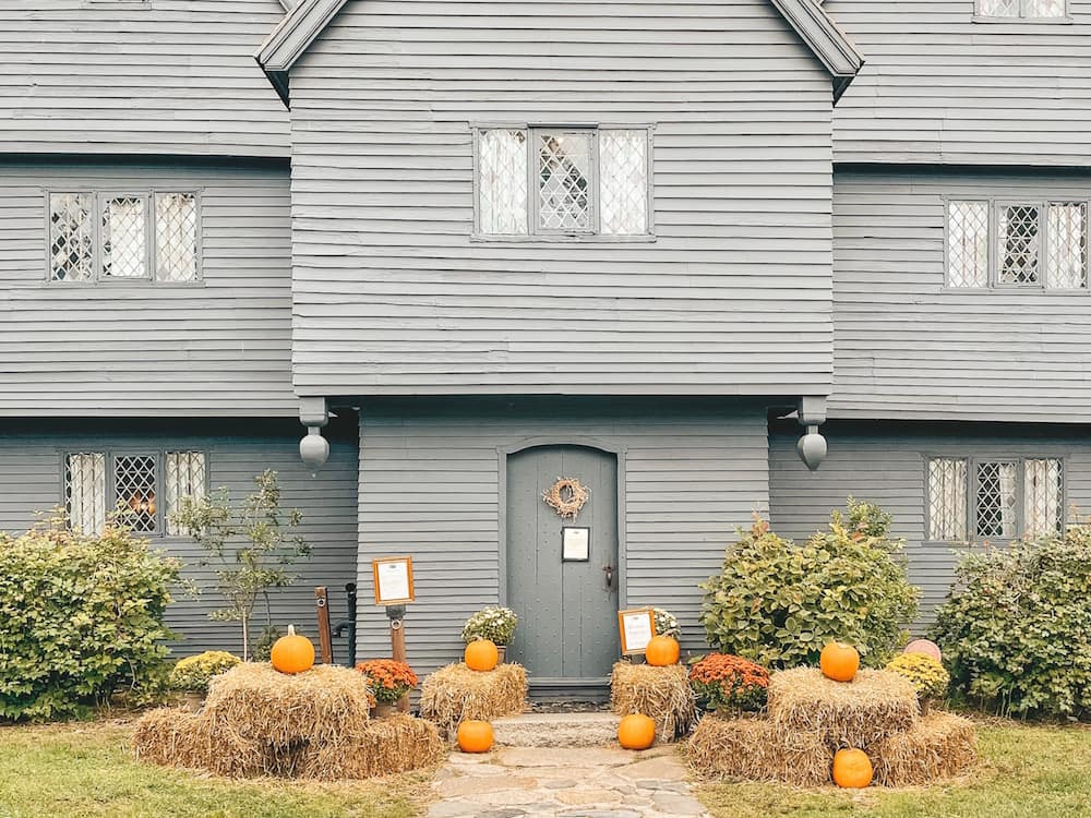 A view of the historic gray The Witch House in Salem in October, with hay bales, pumpkins, and other fall decor on the front porch.