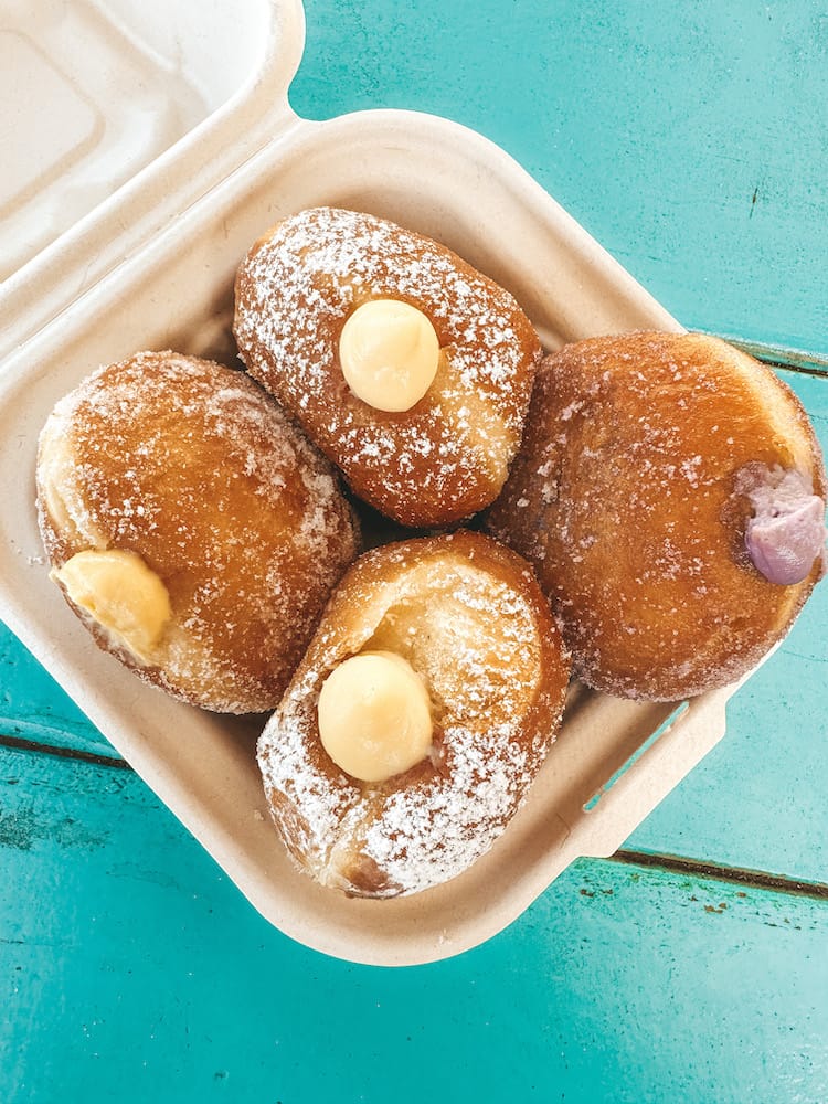A box of four stuffed malasadas on a turquoise wooden table.