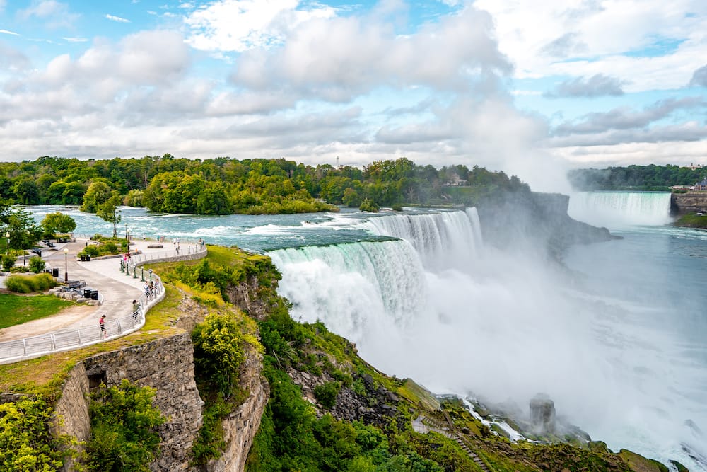Niagara Falls on America side in the morning with clear sky surrounded by lush green foliage with a few onlookers