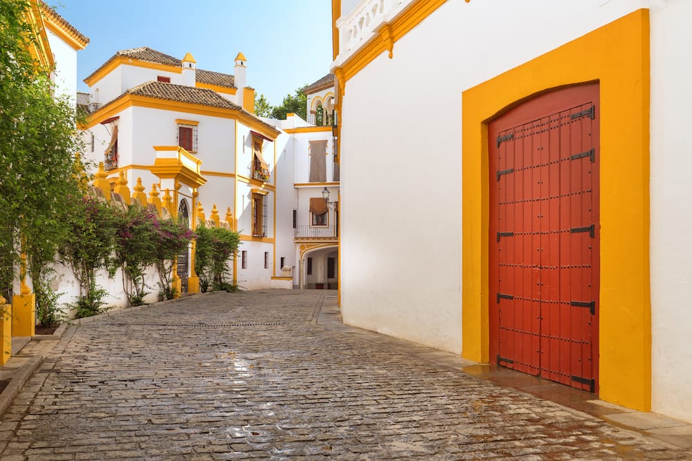 A red door with a yellow frame in a cobblestone street with beautiful white-washed buildings in the Santa Cruz neighborhood in Seville