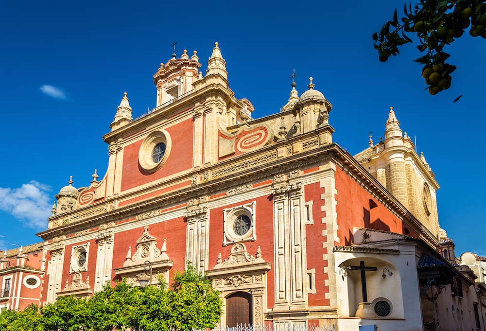 An ornate church with a rust-colored exterior and tan molding against a blue sky in Seville.