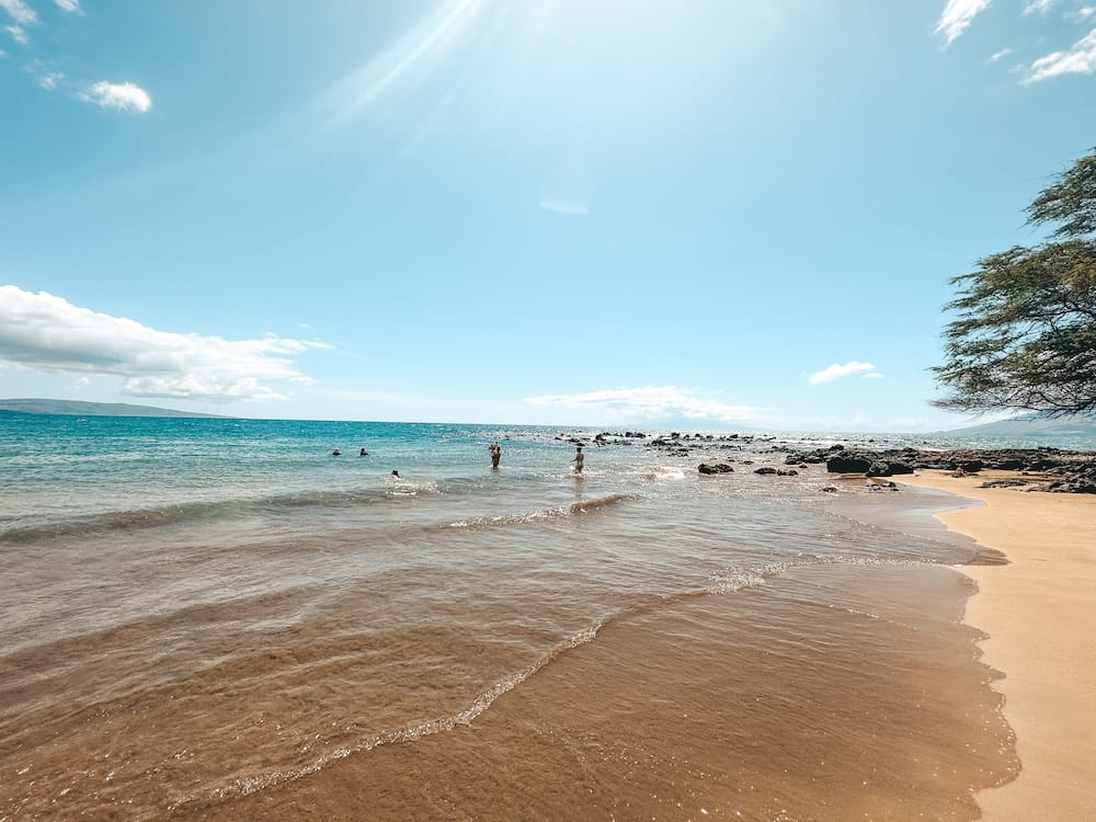 A couple of people are in the water at Ulua Beach, one of the best spots for snorkeling in South Maui.