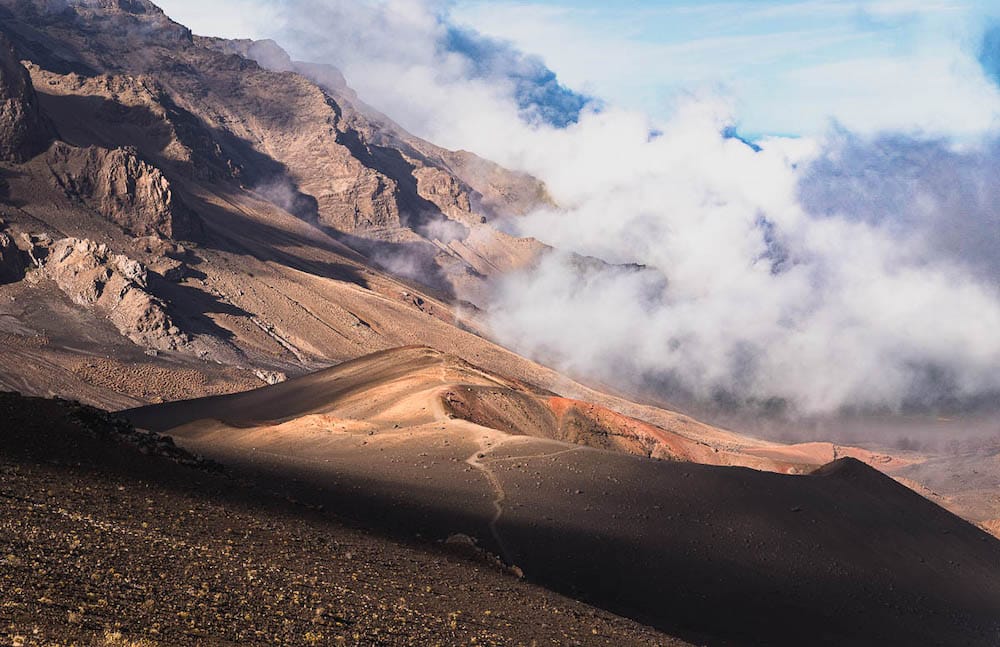 The volcanic terrain and brown and red sand in Haleakalā National Park , with clouds covering the terrain.
