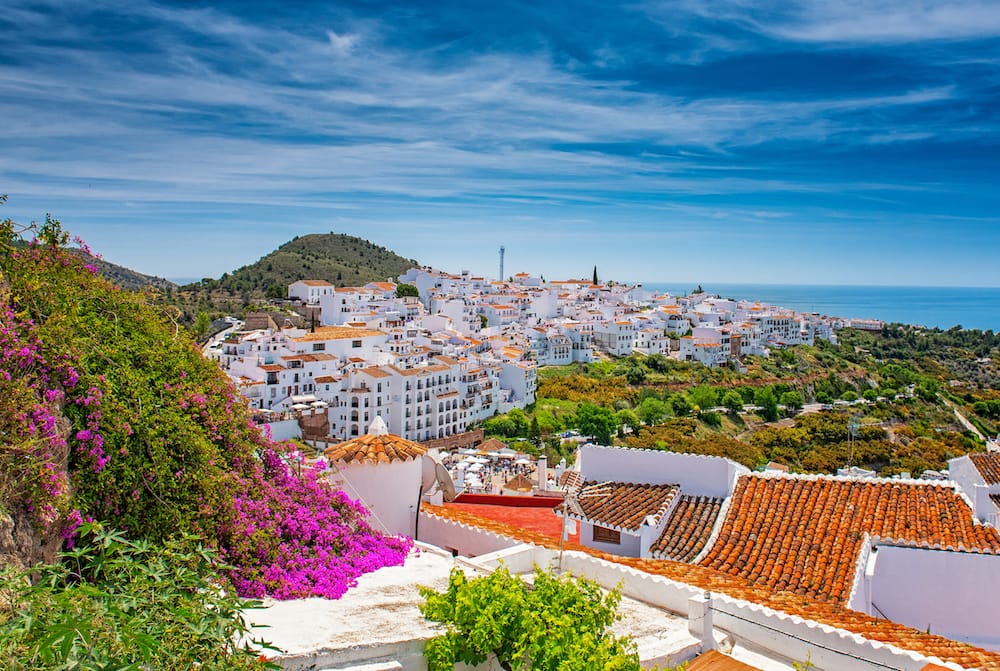 Several white-washed buildings overlooking the ocean with terracotta roofs and pink flowers overlooking the sea in Southern Spain in spring